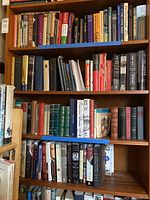 Wide view showing two shelves of a wooden bookshelf filled with multiple hardcover books of various historical and political subjects.
