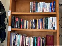 Bookshelf with 3 shelves featuring a diverse collection of books including works by Earlene Fowler, Alan Gordon, Margaret Atwood, Alfred Hitchcock, and others.