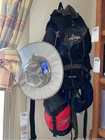 View of camping equipment hanging on a wall including Teton Sports backpack with items attached, Arctic sun hat, and Hyke & Byke sleeping bag