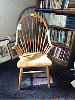 Front view of Windsor-style spindle back wooden chair in front of bookshelf and framed prints.