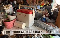 Photo of firewood storage rack assembled with Coleman cooler, baskets, and plastic bags on top