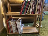 Side view of the wood folding bookshelf showing three shelves with multiple cookbooks and other books placed on the middle and bottom shelves.