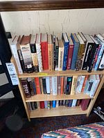 Front view of the folding wooden bookshelf filled with various books of different sizes and colors, set against a textured wall.