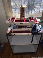 Jewelry box open on top of white cabinet by window, showing red velvet compartments and some decorative items inside