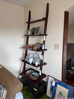 Full view of dark wood leaning bookshelf with five shelves, holding various household items like plates, picture frames, and books for staging only, seller notes contents not included.