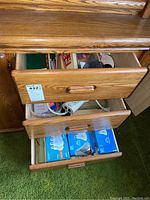 Wooden desk drawer containing English French dictionary, playing cards, power cords, Christmas-themed book, staples, and other supplies