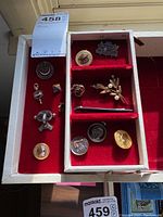 Assorted pins displayed in a red velvet-lined box, showing various designs including floral and emblematic styles.