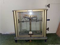 Front view of the vintage balance scale inside glass enclosure showing the weights and mechanism.
