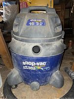 Full view of Shop-Vac contractor style wet/dry vacuum showing large canister, wheels, and handle, dusty from storage.