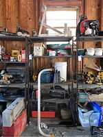Wide view of shelves with various tools including power tools, toolbox, fishing tackle, and hardware items arranged on metal shelving.