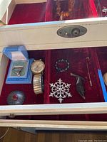 Helbros wristwatch with metal band, black beaded ring, snowflake pin, red stone pin, arrow hat pin, and two other pins displayed in red velvet-lined case.