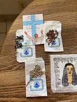 All three rosaries displayed on original Galleria Savelli packaging, with prayer card and mantilla on table.