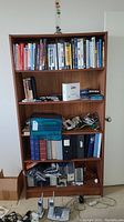 Front view of wooden bookshelf filled with books, binders, and electronic items.