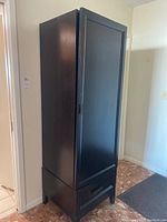 Photo of the full black wooden cabinet showing closed door, lower drawer, and overall structure.