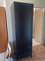 Full view of closed black wooden cabinet showing overall shape, drawer at bottom, and door design.