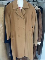 Tan wool double-breasted women's coat hanging on clothing rack