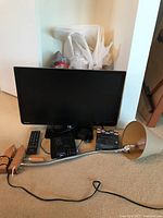 Overall view of Toshiba 23 inch TV with included remote, Roku XD streaming device, Fire TV stick, power adapters, and clamp lamp with beige shade.