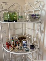Photo of various items on a white metal shelf including green and clear drinking glasses, two beer steins, several figurines, and a small metal bowl.