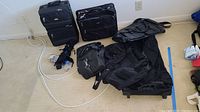 Photo showing multiple pieces of luggage including two rolling suitcases, a duffel bag, a shoulder bag, and two luggage locks on the floor.