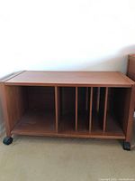 Front view of wooden media cart with vertical dividers and caster wheels on floor
