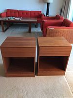 Front view of two teak nightstands on carpet with red sofa in background