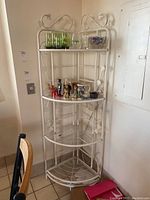 Full view of the white corner shelving unit showing its four shelves and decorative leaf design on the metal sides and top.