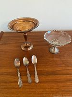 Photo showing entire lot of two candy dishes and three teaspoons on a wooden surface.