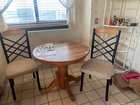 Full view of the round wooden pedestal table with two metal-framed chairs with wooden backrests and beige upholstered seats.