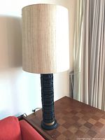 Front view of the table lamp featuring the tall beige fabric shade and black textured base with gold accent on a wooden table.