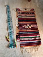 Photo showing the Navajo rug with multi-colored horizontal stripes and central diamond, next to the two tapestries, one turquoise floral and one beige with black and pink designs.