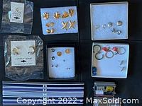 Overview of assorted sets of earrings arranged in boxes and packaging on a dark surface.