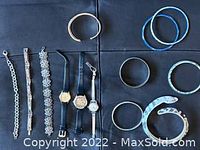 Photo showing three wristwatches and seven bracelets arranged on a black surface.