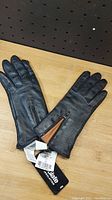 Front side of black Danier leather gloves showing zippered wrist detail and tags
