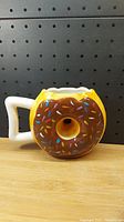 Front view of donut-shaped coffee mug with chocolate frosting and colorful sprinkles, showing handle and flat bottom.
