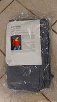 Packaged folded solid muslin fabric background in thunder gray with brand label amvona visible.