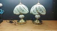 Pair of brass and white glass table lamps with floral designs on a wooden surface
