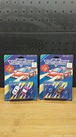 Front view of two sealed Micro Machines Super Street Machines blister packs, one with a white car and one with a pink car.