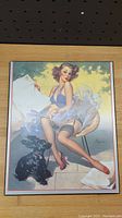 Front view of pinup girl wood picture showing woman in blue top, stockings, and red shoes with a dog at her feet.