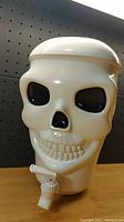 Front view of the white plastic skull-shaped drink dispenser with black hollow eyes and nose, showing the tap and teeth details.
