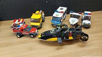 Top view of six assembled small building block vehicles on wooden surface against black pegboard background