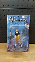 Front view of the Greasers figurine in original packaging showing female figurine and branded card.