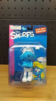 Front view of one sealed Smurf figure in original packaging with blue and pink cardboard backing and clear blister.