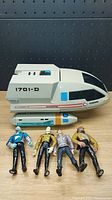 Photo of white and gray Star Trek shuttlecraft model 1701-D with four Star Trek action figures displayed in front on a wooden surface.