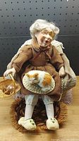 Porcelain figurine of an elderly woman seated in a chair holding a basket, with a small sleeping cat on her lap.