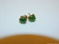 Front angled view of pair of vintage round jade stone stud earrings in 10 karat gold six-prong setting on a white background.