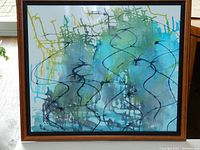 Abstract watercolour painting with blue, green, black, and yellow details in wooden frame with beveled brown edge and black twisted rope inner edge.