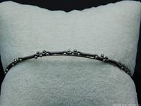 Close-up image of the bangle resting on a white pillow, showing the metal bead clusters and silver coils wrapped around the band.