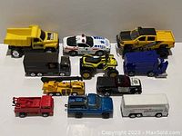 Overview of 11 small toy trucks and working vehicles arranged on flat surface, showing varied colors and types.