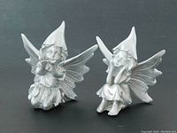 Two silver finish flower fairy statues on dark background showing front and side angles, both standing and sitting fairies visible.