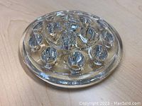 Clear thick glass flower frog displayed on wooden surface, showing multiple rounded holes.